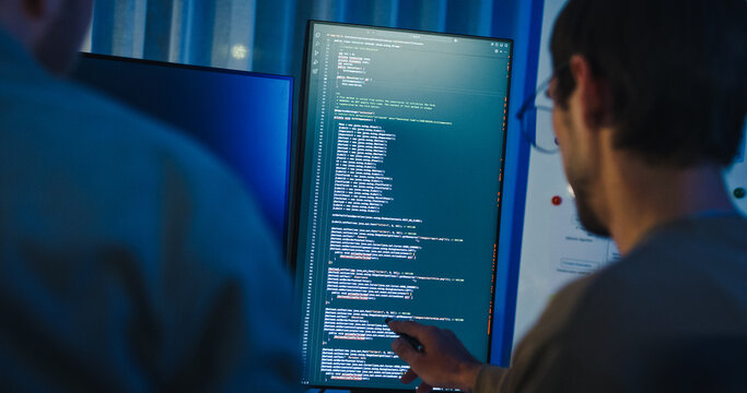 Closeup team adult male engineer collaborate on robotic hand project use AI code solutions machine learn at tech workspace night. Artificial intelligence interface collaboration prototype development.