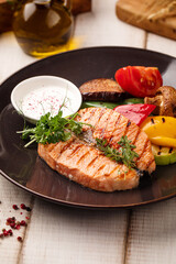 Juicy grilled salmon fillet served with fresh vegetables, sauce and herbs on a dark plate