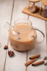 Warm milk tea brewed with star anise and cinnamon served in a clear glass teapot on wooden table