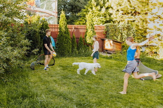 Teens and children playing football together with dog in summer backyard