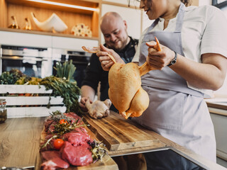 Chef holding raw chicken beside venison meat during cooking class in kitchen
