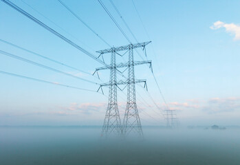 Power lines and transmission towers with ground fog at sunrise in Netherlands