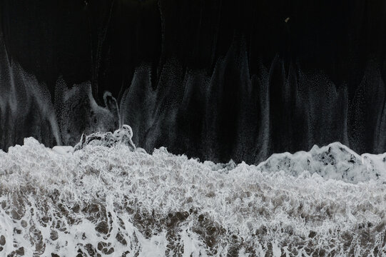 Top view of crashing waves on a dark sandy beach in Asturias