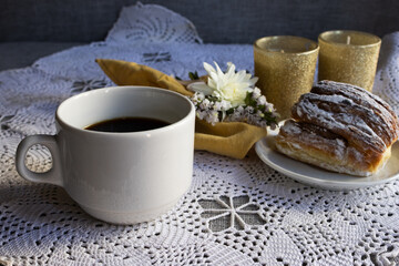 Side view of a set with coffe and pastry served on a white tablecloth with white flowers and...