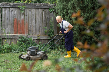 Gardening and country life. Banner. A man with a lawn mower is mowing the grass in the backyard....