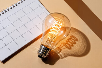 A calendar and a lit lightbulb on a beige surface suggesting planning and creative ideas together