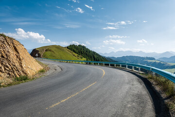 Empty curving asphalt road running through the beautiful green mountain landscape under a clear blue sky.