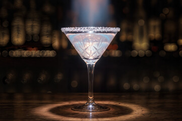 Elegant martini glass with sugared rim illuminated on a wooden bar with a blurred background