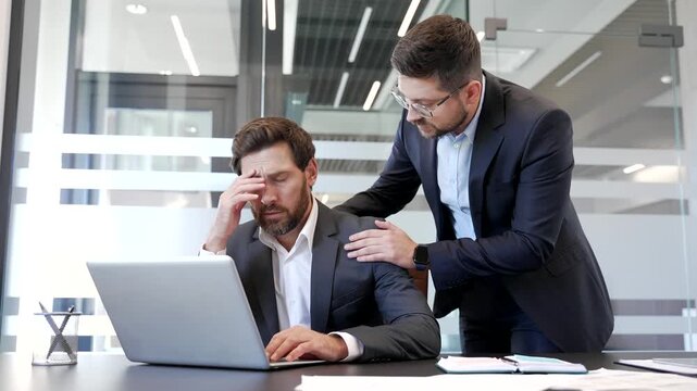 Businessman supports stressed colleague at workplace in business office. Male coworker supporting upset worried friend in depression and problems at work. Manager comforting employee with mental pain