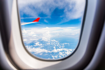 Obraz premium Scenic view through an airplane window showing the white wing and red tip against a clear blue sky,