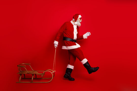 Jolly Santa Claus in festive attire pulling a wooden sleigh against a bright red background, radiating holiday joy
