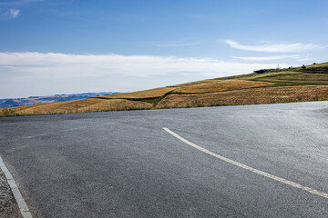 Empty road with asphalt and golden hills under a blue sky.