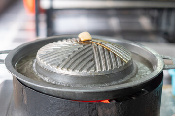 Close-up of Thai-style barbecue grill pan, known as Moo Kratha, with pork belly, shrimp, and vegetables cooking on a hot grill and soup. Popular Asian dining experience in Thailand.