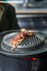 Close-up of Thai-style barbecue grill pan, known as Moo Kratha, with pork belly, shrimp, and vegetables cooking on a hot grill and soup. Popular Asian dining experience in Thailand.