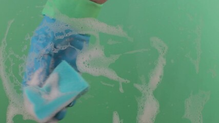 A hand in a rubber glove cleans a dirty surface. The hand cleans glass with a scrubbing sponge. Chroma key background. Concept of housework and cleaning.
