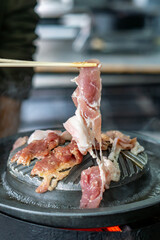 Close-up of Thai-style barbecue grill pan, known as Moo Kratha, with pork belly, shrimp, and vegetables cooking on a hot grill and soup. Popular Asian dining experience in Thailand.