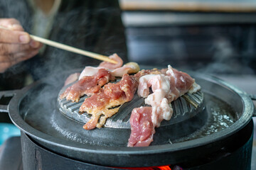 Close-up of Thai-style barbecue grill pan, known as Moo Kratha, with pork belly, shrimp, and vegetables cooking on a hot grill and soup. Popular Asian dining experience in Thailand.