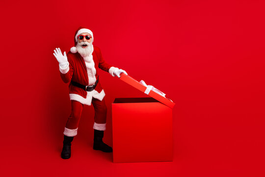 Festive Santa Claus opening a gift box on red background celebrating Christmas and spreading holiday cheer