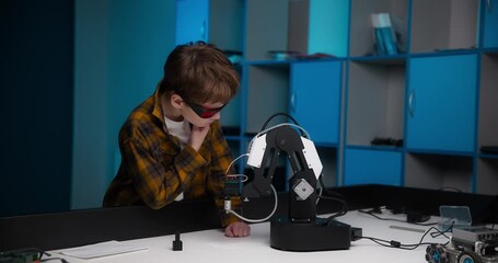 A bright Caucasian 10-year-old boy with glasses looks thoughtfully at a robotic arm. concept of stem education - Powered by Adobe