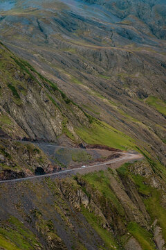 A white SUV drives along the winding Abano Pass road in Tusheti, Georgia, surrounded by steep rocky slopes and dramatic mountain terrain