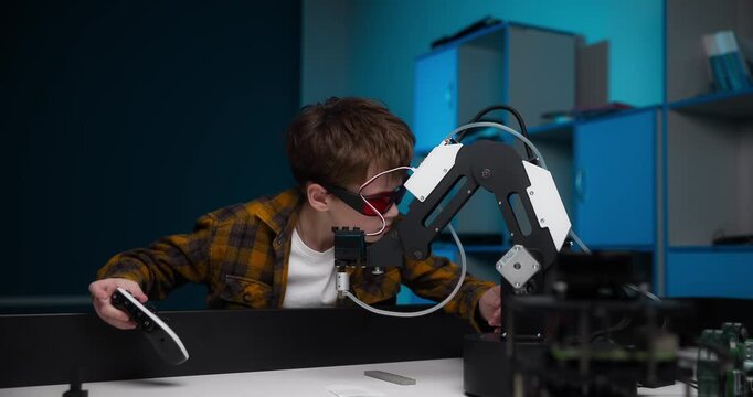A 10-year-old Caucasian teenager checks a robotic arm by wearing special red glasses. A boy with white skin participates in a STEM education program science, technology, engineering