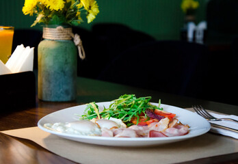 Classic breakfast plate featuring fried eggs, crispy bacon, fresh greens, and sliced tomatoes served on a white dish.