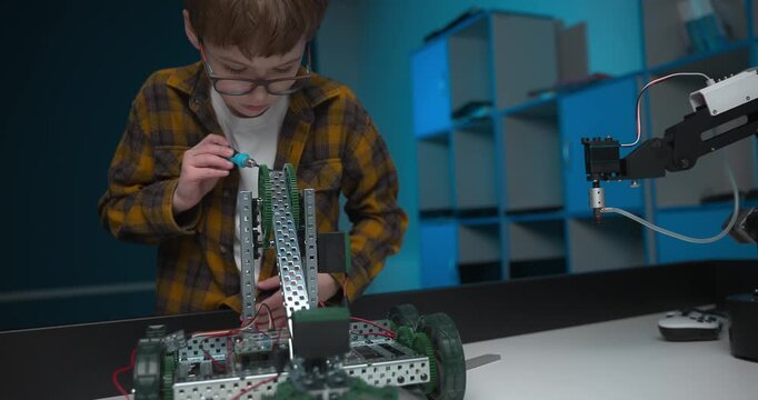 A young Caucasian boy is engaged in a robotics lesson, holding a screwdriver in his hands, repairing a robotic constructor. The concept of the STEM Science, Technology, Engineering