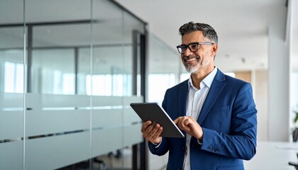 Smiling senior Latin businessman using tablet computer in modern office