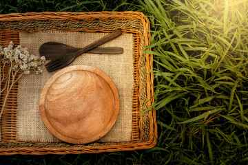 A round wooden plate placed on burlap inside a rustic wicker basket, surrounded by green leaves and natural sunlight, creating a warm, organic, and eco-friendly backdrop ideal for food, nature