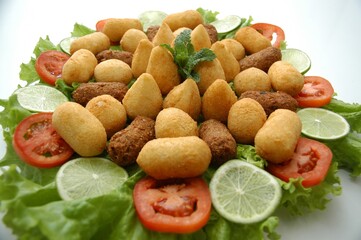 Flat lay of a Brazilian appetizer platter with fried snacks, lettuce, tomato, and lime. Perfect for food blogs, menus, or party planning content.
