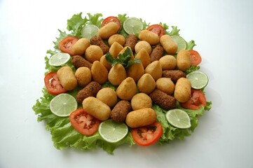 Flat lay of a Brazilian appetizer platter with fried snacks, lettuce, tomato, and lime. Perfect for food blogs, menus, or party planning content.
