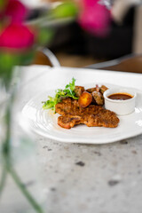 pan-fried veal cutlet (Milanese or schnitzel style), roasted potatoes, a side salad, and a small white ramekin of sauce on a white plate in a restaurant setting.