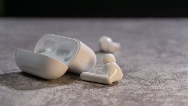 White wireless earbuds and an open charging case displayed on a textured table, captured with shallow depth of field to emphasize product detail and sleek everyday audio