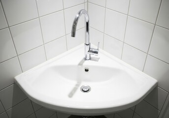 Fototapeta premium Modern white corner sink with chrome faucet in a tiled bathroom.
