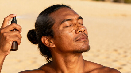 Relaxing Polynesian man enjoying self care with facial mist at a serene spa setting. Cosmetics advertising