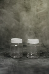Two clear plastic jars with white lids displayed on a textured gray surface. This simple and clean mockup is ideal for product packaging previews, branding concepts, storage container designs