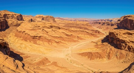 Fototapeta premium Expansive panoramic view captures layered rock formations within a sunlit arid canyon landscape under a clear blue sky