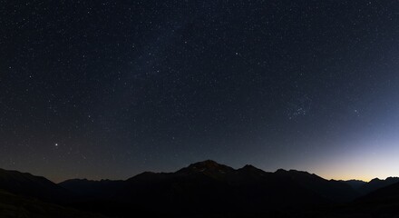 無数の星が輝く暗い夜空の下広がる雄大な山並み地平線に淡く光る遠景が静かな夜を彩る. AI Generated