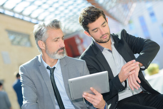 businessmen holding tablet and looking at watch