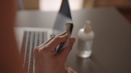 Close-up of unrecognizable person wiping dusty laptop screen with microfiber cloth after spraying cleaning solution, promoting hygiene and proper electronic device maintenance for optimal performance.