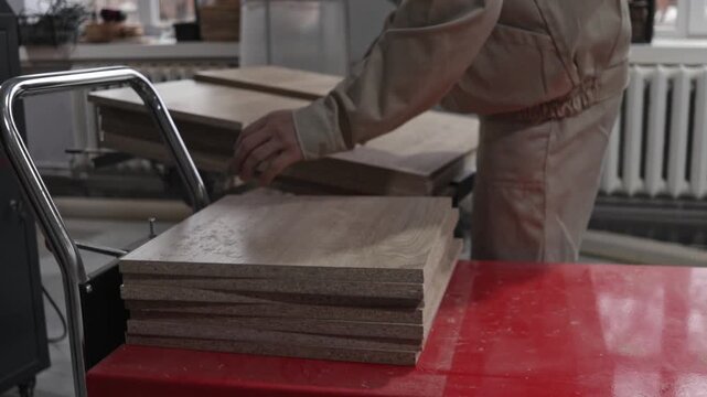 Close-up of the hands of a craftsman who assembles freshly cut chipboard panels in a carpentry workshop, preparing materials for further furniture production.
