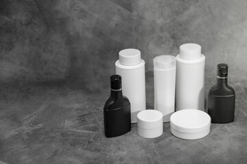 A collection of white and black cosmetic containers arranged on a dark platform with a textured gray background.