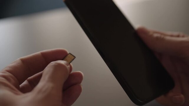 Detail cropped shot of unrecognizable man inserting nano sim card into new smartphone tray sitting on desk, illustrating mobile service transfer, setup, and device upgrade connectivity, slow motion.