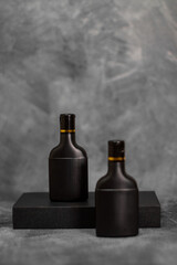 Two elegant black cosmetic bottles standing against a textured gray background. This minimalist mockup is perfect for branding, product packaging previews, advertising materials, and modern design