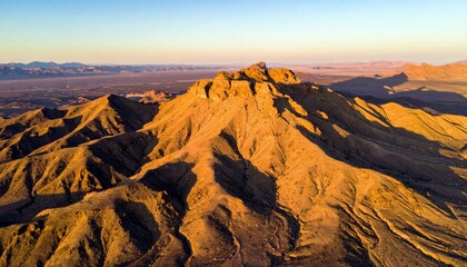 An aerial view of a vast mountain range illuminated by the warm, golden light of the setting sun.