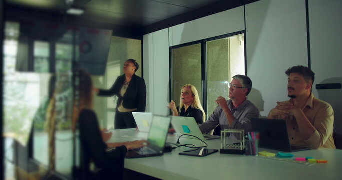 African American businesswoman answering questions during team presentation while colleagues engage and observe in modern office conference room