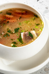 delicious fish soup served in a white bowl on a white plate, featuring large salmon pieces, carrots, and fresh herbs.