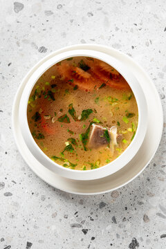 delicious fish soup served in a white bowl on a white plate, featuring large salmon pieces, carrots, and fresh herbs.