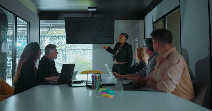 African American businesswoman explaining data during team presentation as colleagues look on in well lit modern conference room - Powered by Adobe