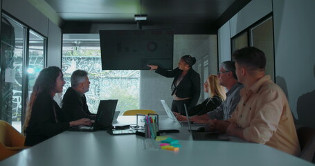 African American businesswoman explaining data during team presentation as colleagues look on in well lit modern conference room